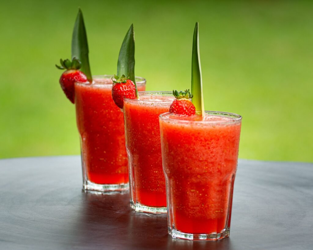 Vibrant strawberry smoothies garnished with pineapple leaves, perfect for summer refreshment.